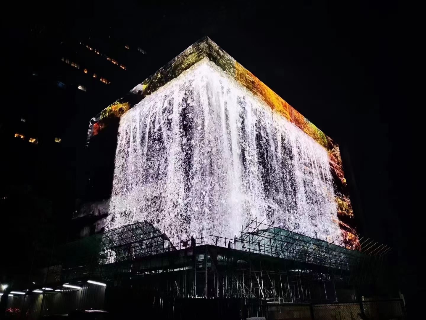 Building corner LED display showing a dramatic waterfall cascading down the facade