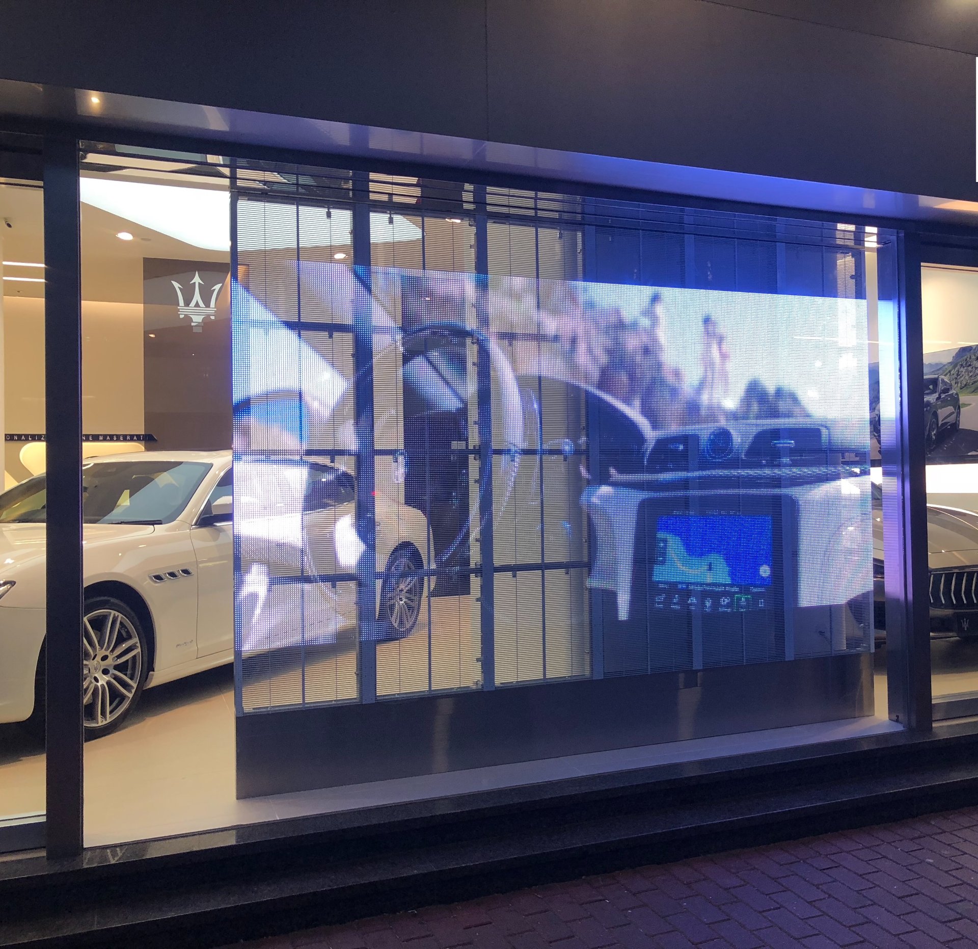 Transparent LED screen in a Maserati showroom window displaying automotive content